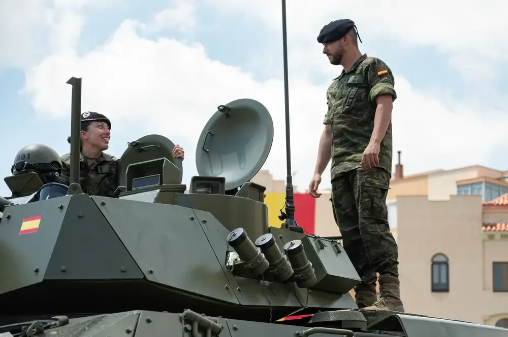 Dos militares españoles con uniforme de camuflaje sobre un vehículo blindado durante un desfile