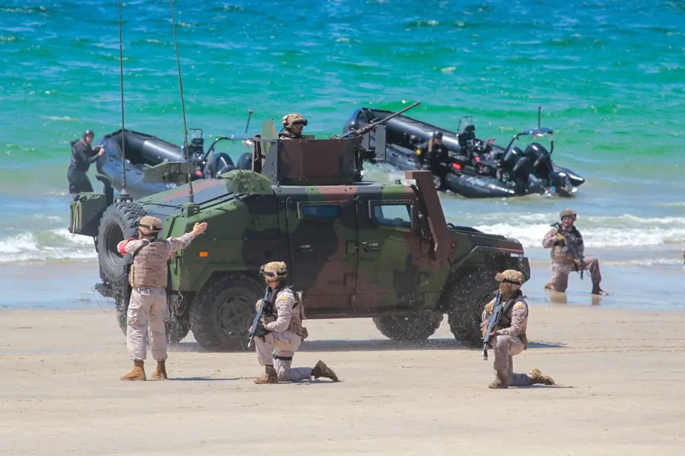Candidatos a militares realizando un ejercicio táctico de resistencia con vehículos blindados en una playa.