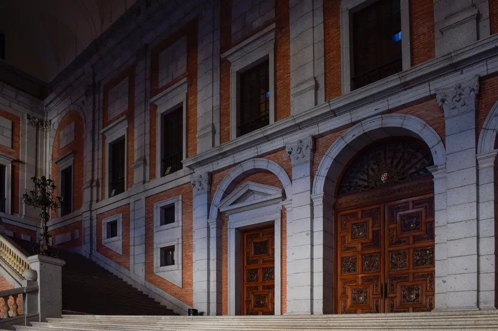 Fachada de piedra y ladrillo de un edificio histórico con grandes puertas de madera tallada y arcos monumentales.