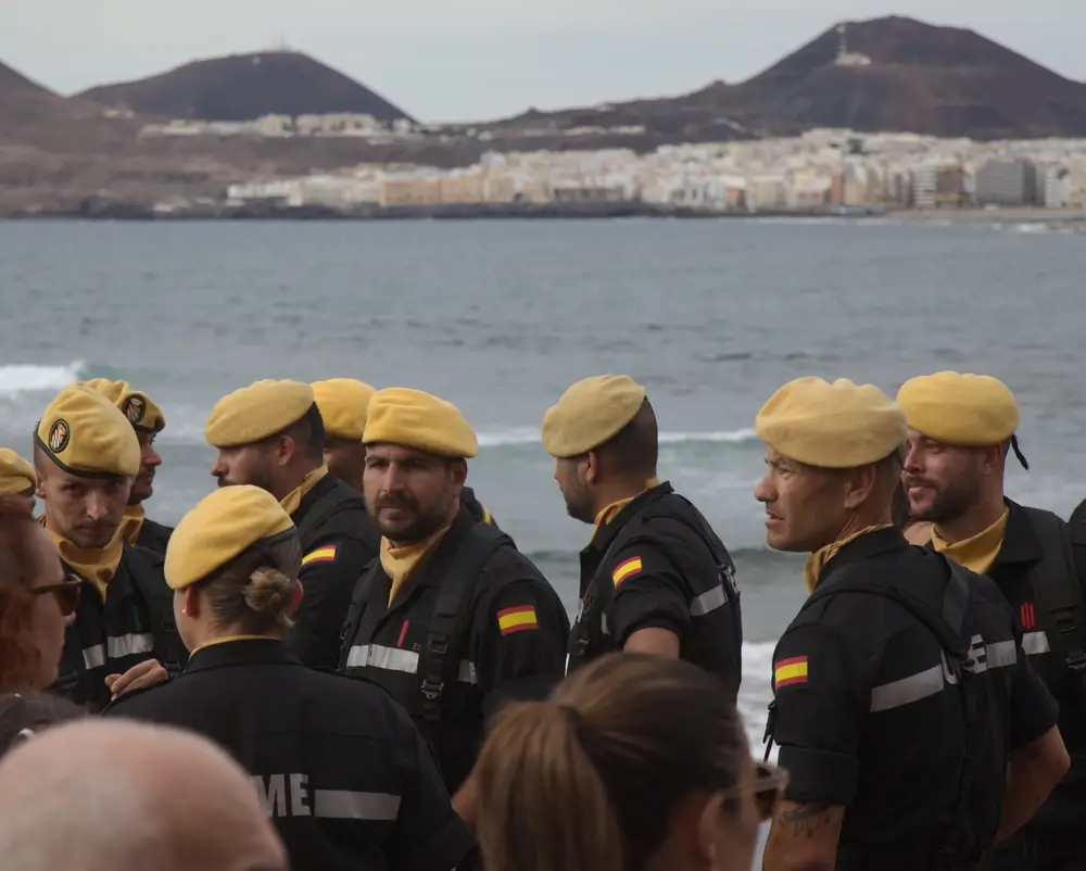 Soldados jóvenes españoles con boina amarilla y uniforme oscuro durante un entrenamiento militar en la costa.