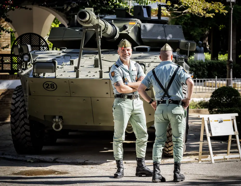 Suboficiales del Ejército de Tierra español uniformados frente a un vehículo blindado durante una jornada de instrucción.