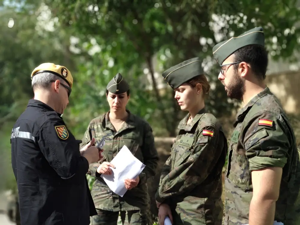 Reservista voluntario y militares profesionales españoles trabajan en equipo revisando un documento al aire libre.