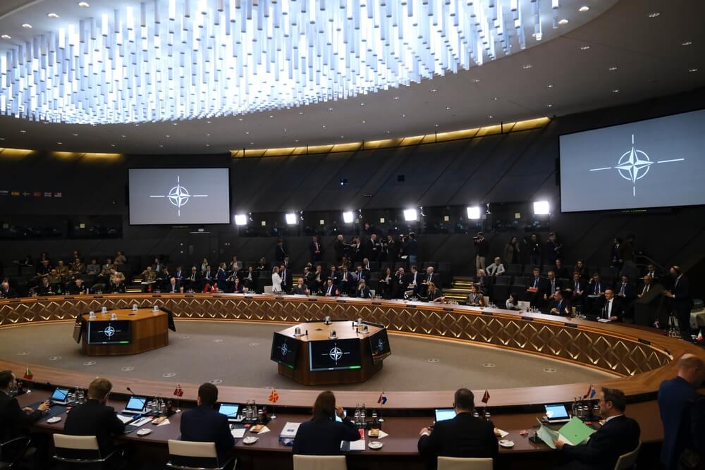 Réunion militaire de défense de l'OTAN dans une salle circulaire avec des écrans affichant le logo de l'alliance.