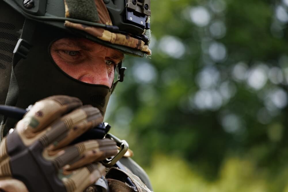 Operador militar con casco y pasamontañas hablando por radio en el campo para una comunicación táctica clara.