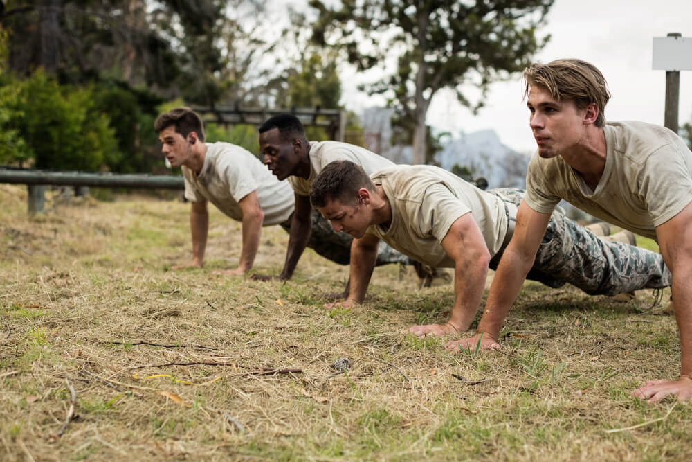Soldados realizan flexiones sobre el césped para mejorar su fuerza y técnica durante un entrenamiento físico militar.