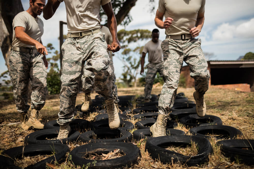 Aspirantes militares corriendo entre neumáticos en un circuito de agilidad y resistencia física al aire libre.