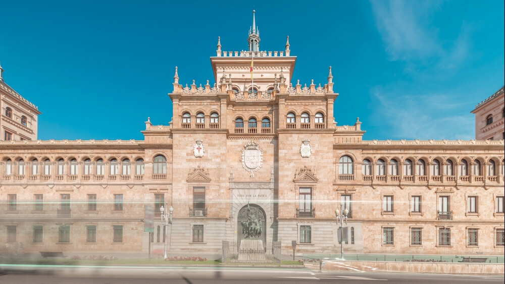Fachada de una academia militar española con bandera nacional y patio de formaciones