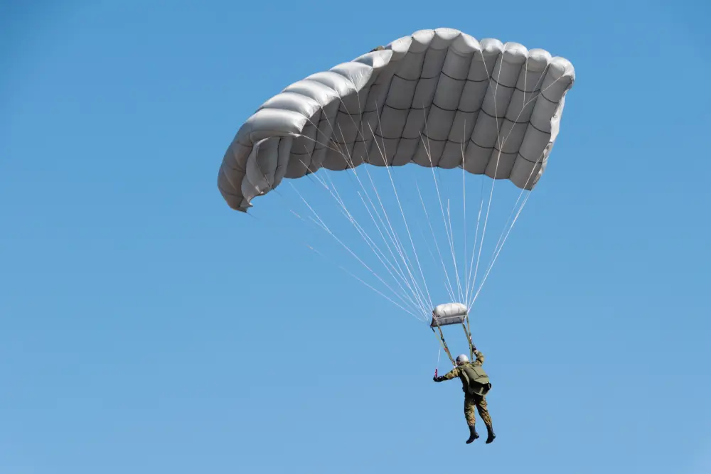 Paracaidista de la BRIPAC con equipamiento táctico militar descendiendo bajo un paracaídas en un cielo azul despejado.