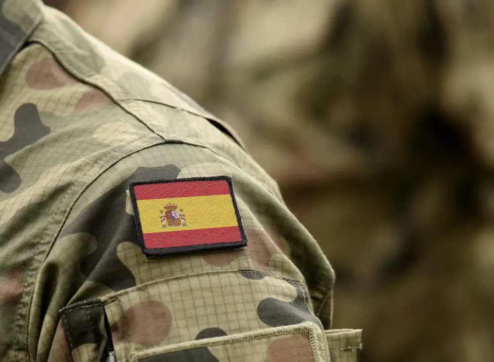 Bandera de España en la manga de un uniforme castrense de camuflaje, detalle de las insignias y divisas militares.