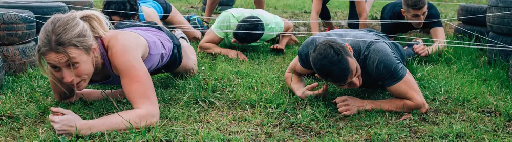 Aspirantes militares realizan pruebas físicas de resistencia gateando bajo obstáculos en un entrenamiento al aire libre.