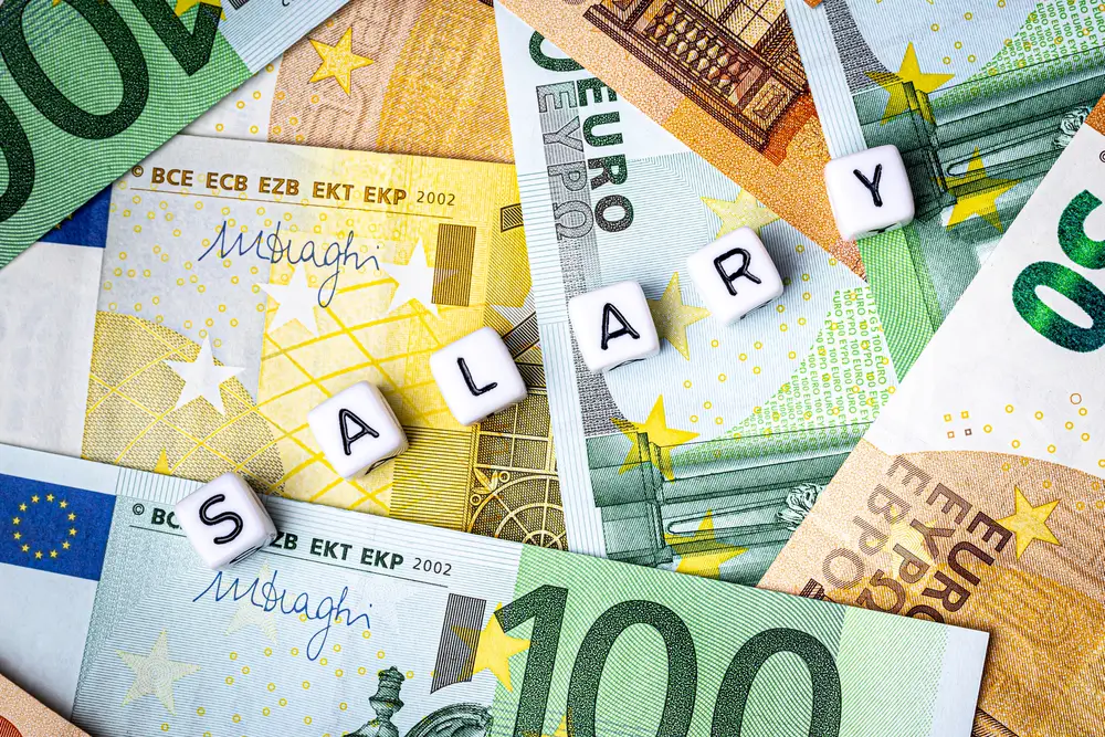 Billetes de euro con dados que forman la palabra SALARY, ilustrando el sueldo y la nómina de un militar.