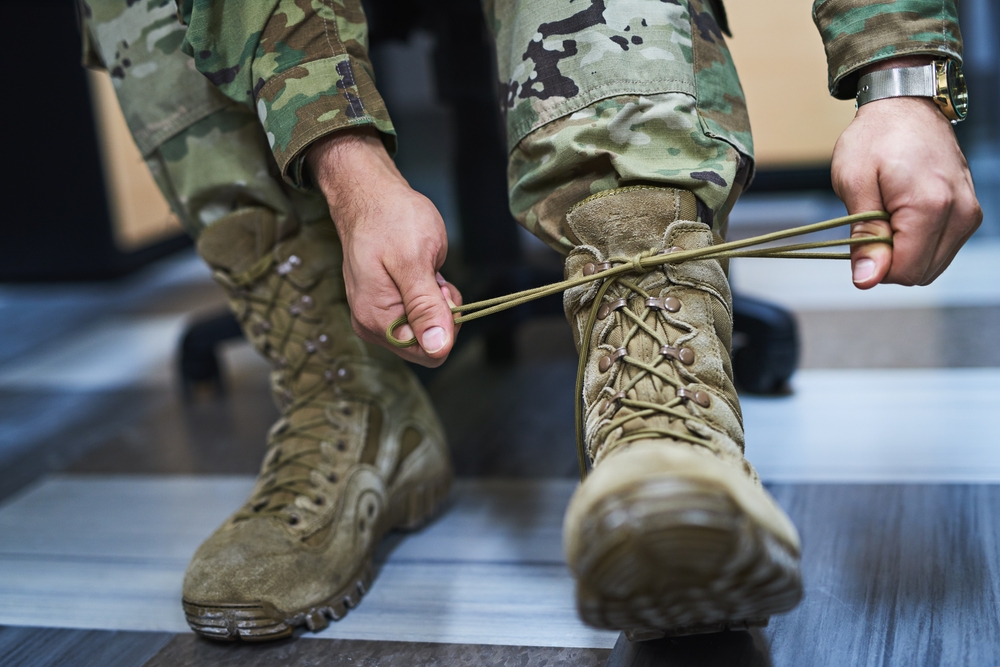 Soldado profesional ajustando sus botas militares con uniforme de camuflaje para la convocatoria de Tropa y Marinería.