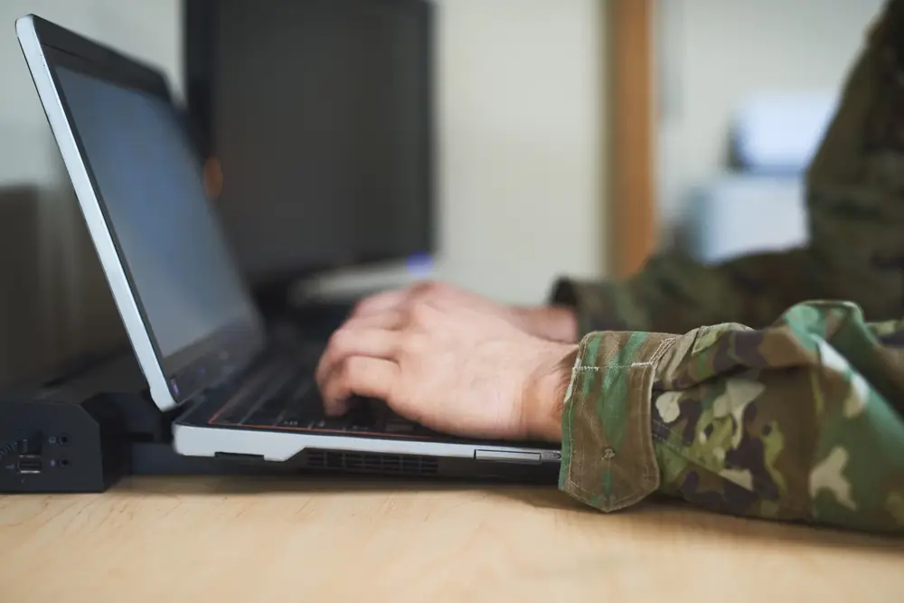 Militar gestionando documentación oficial y formularios de solicitud para las oposiciones en un ordenador portátil.