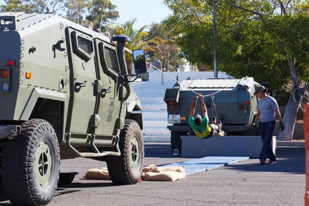 Aspirante realizando ejercicio de cuerda entre vehículos militares durante las pruebas físicas de acceso al ejército.