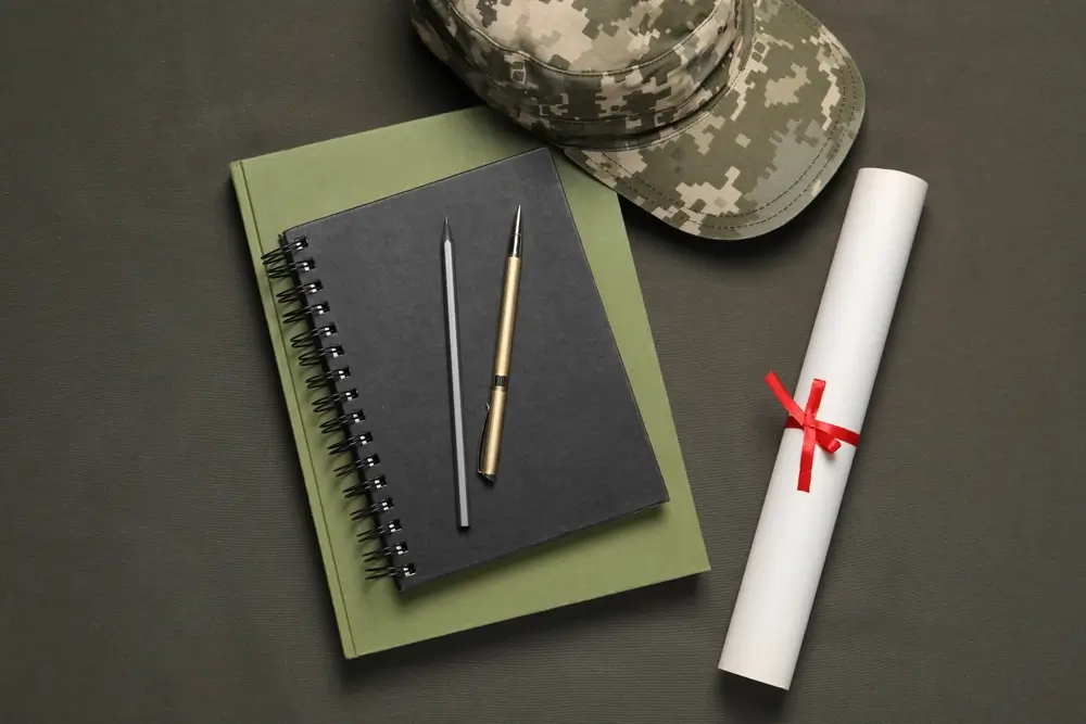 Gorra militar, cuadernos y diploma sobre un escritorio, representando el estudio y formación de un estudiante militar.