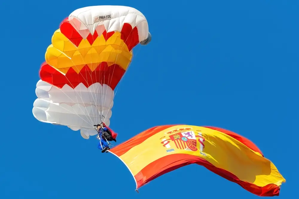 Paracaidista de la BRIPAC descendiendo con la bandera de España, símbolo de la unidad aerotransportada del Ejército.