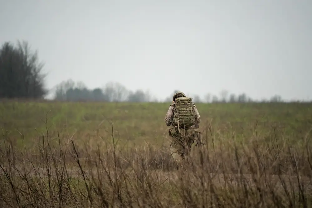 Legionario con equipo de combate y mochila avanzando por el campo durante un ejercicio táctico de infantería.