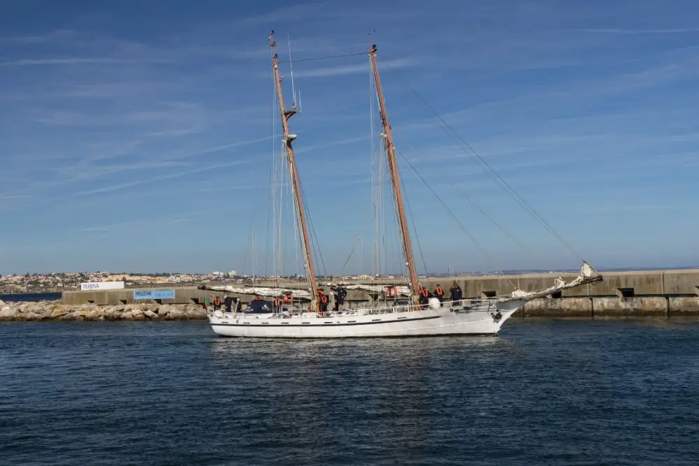 Buque escuela de vela de la Armada navegando frente a un espigón durante un crucero de instrucción naval.