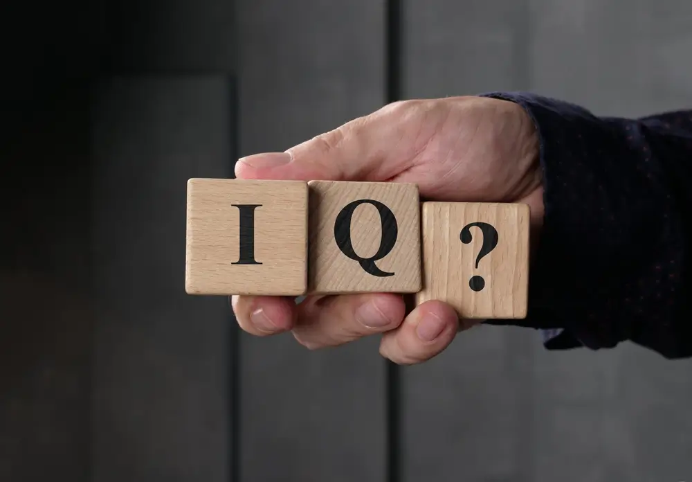 Mano sosteniendo cubos de madera con IQ? para representar un test de aptitudes cognitivas y razonamiento lógico.