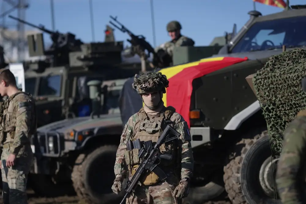 Soldado de fuerzas especiales armado frente a vehículos blindados durante un ejercicio multinacional de la OTAN.