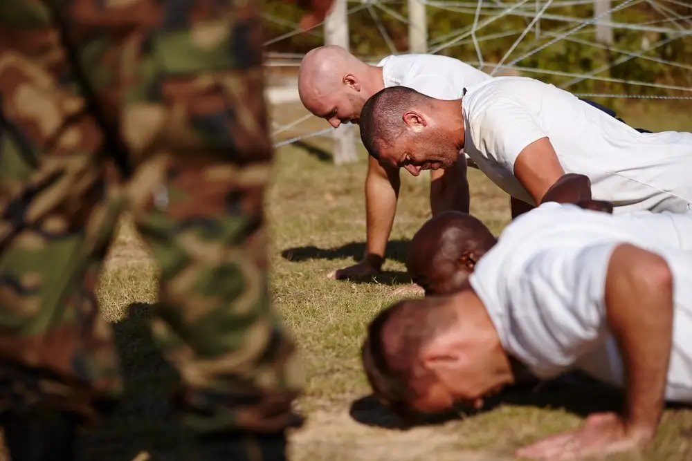 Reclutas haciendo flexiones en el suelo durante un entrenamiento físico de formación militar al aire libre.